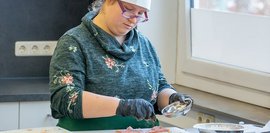 Bildgalerie: Junge Frau in einer Küche mit Kochmütze und Kochschürze würzt Fleisch.